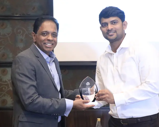 A teammate in a white shirt receiving a crystal trophy for eight years of service