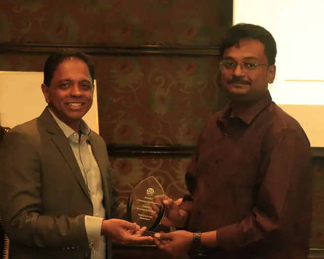 A teammate in a maroon shirt receiving a crystal trophy for eight years of service