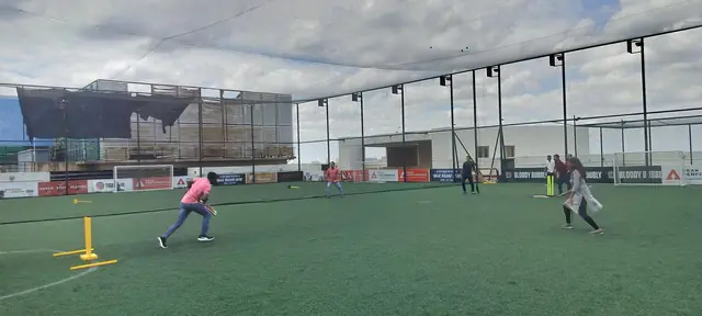 Box cricket on a netted rooftop pitch, one player running between the stumps