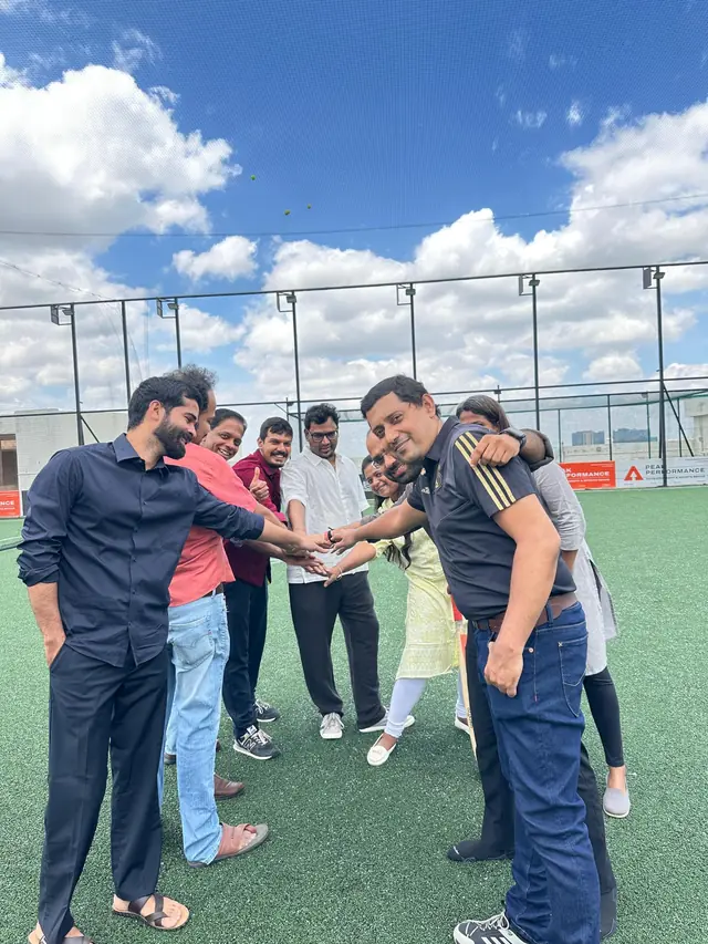 Teammates in a circle on a rooftop turf pitch, hands stacked together in the middle